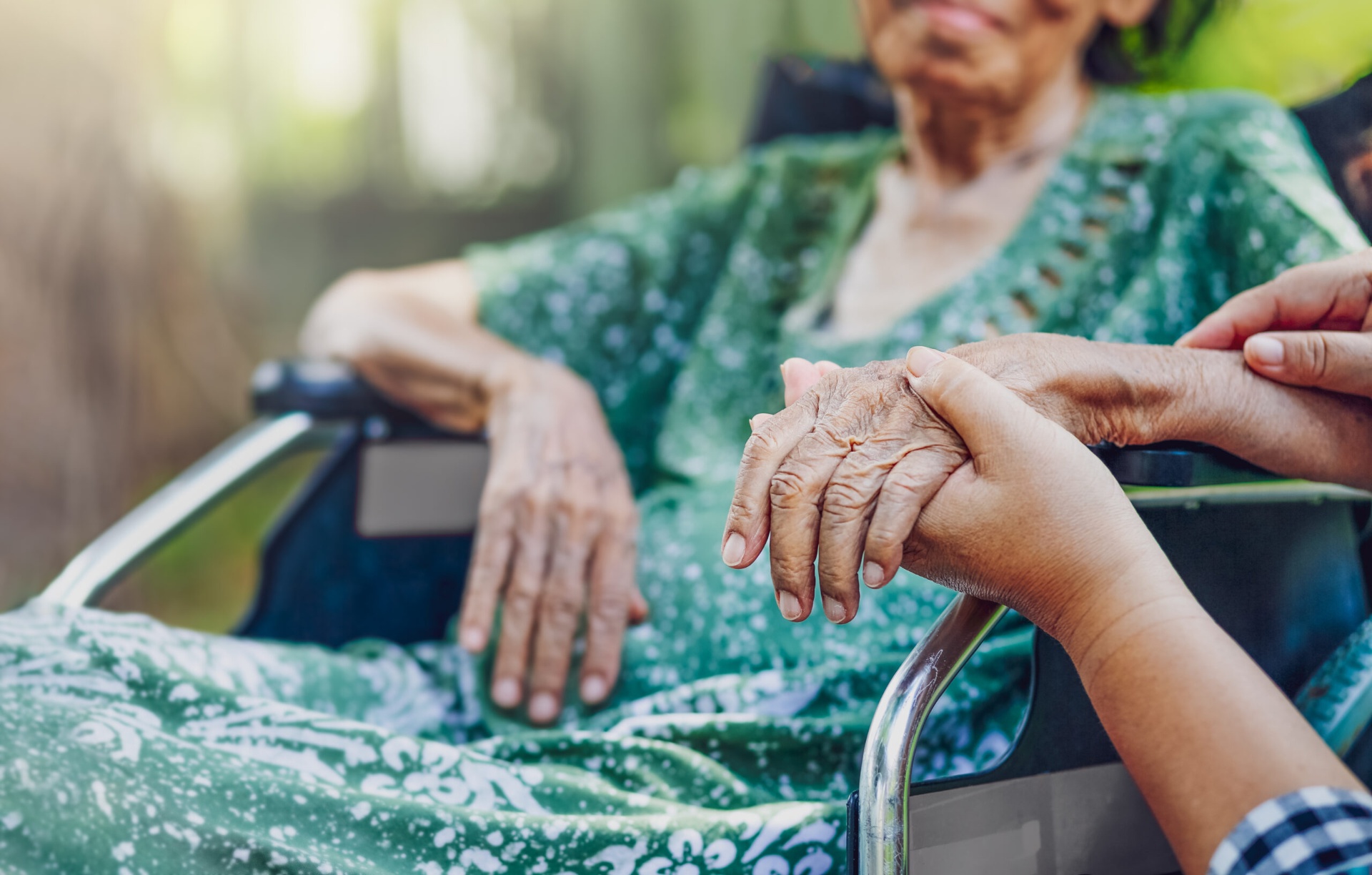 Caring caretaker holding the hand of an elderly dialysis patient seated in a wheelchair