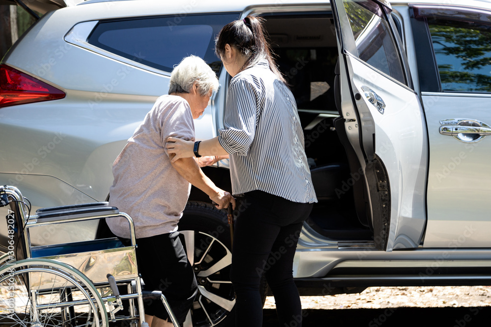Caregiver helping elderly Asian woman into car
