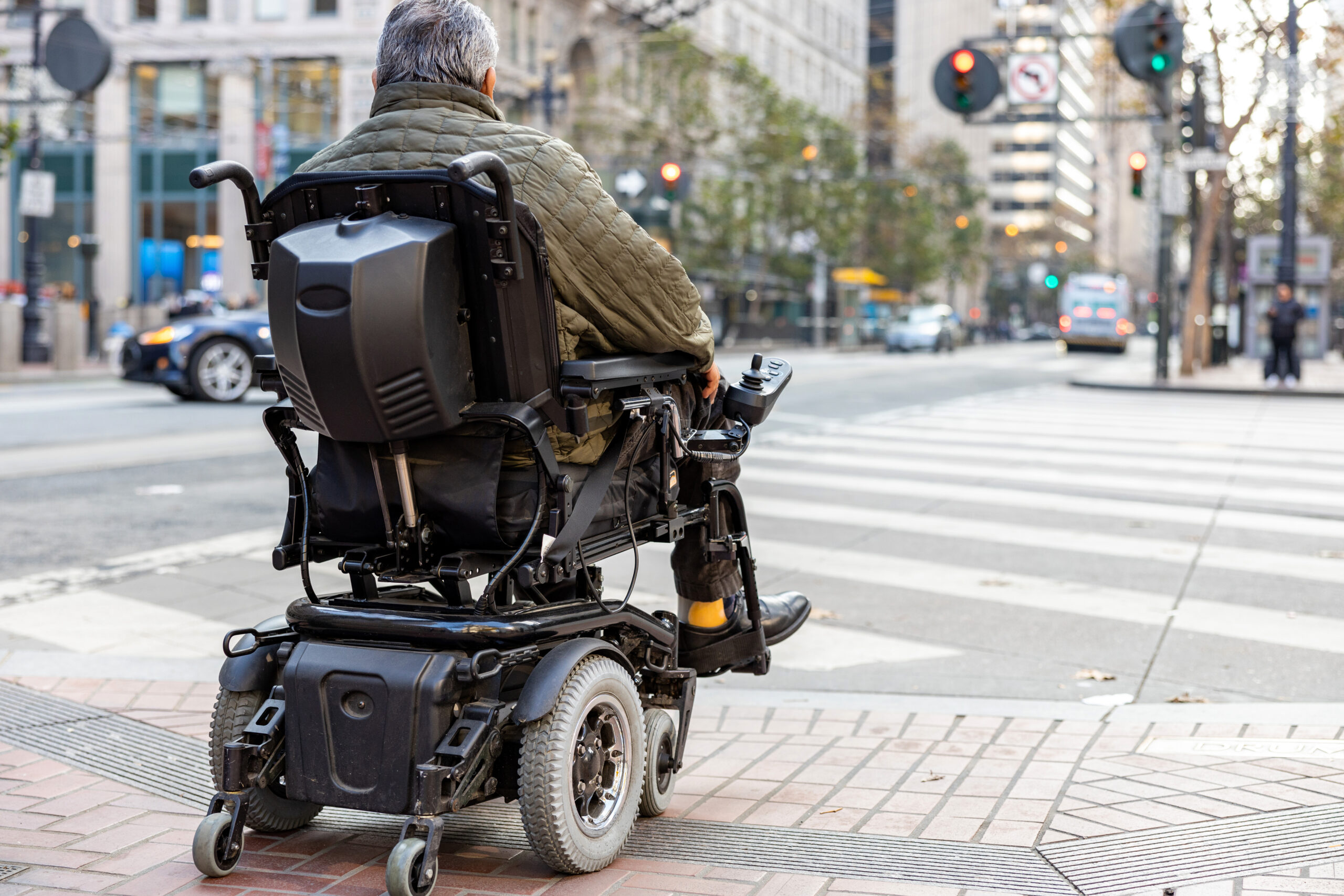 An elderly disabled person on an electric wheelchair on a city street in front of a pedestrian crossing.
